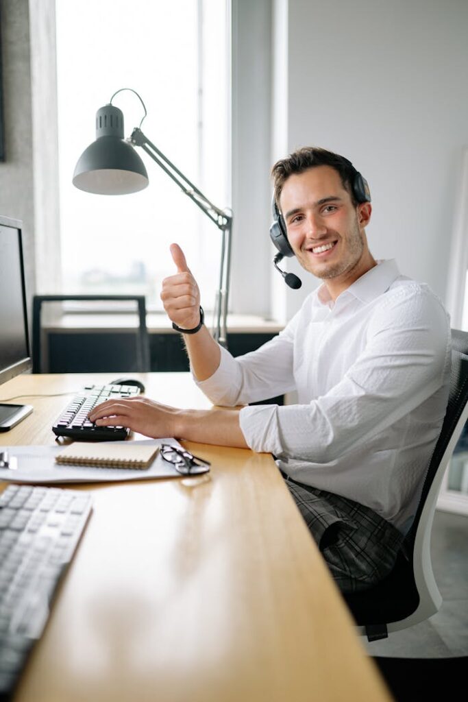 pexels-photo-8867433 Friendly customer service agent wearing headset and smiling with a thumbs up at a modern office desk.